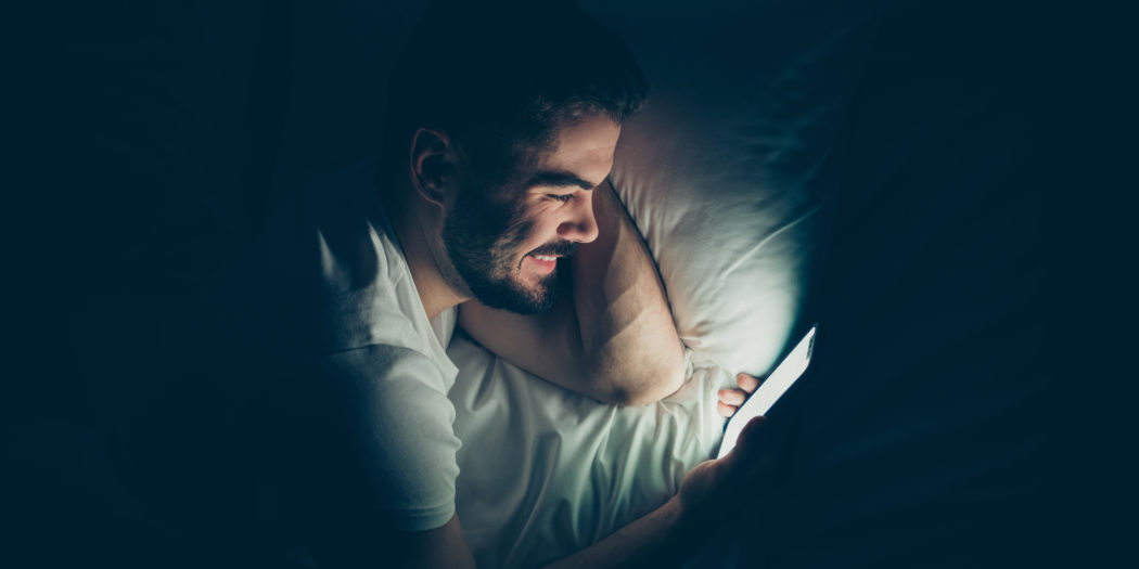 mężczyzna wpatrzony nocą w ekran smartfona